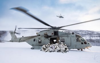 A group of men in white huddle next to a helicopter which is on the ground in a snowy landscape
