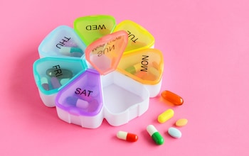 Various pills and pill box on pink background